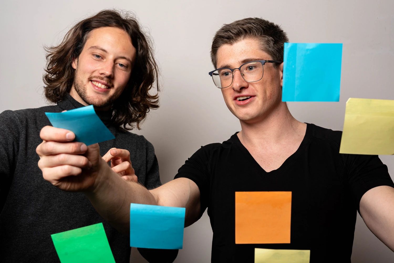 Teamfoto CodingBase. 2 Personen lachen, während Sie Post-Its in einem Workshop ankleben.